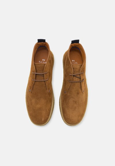 Braune Wildleder-Ankleboots mit Schnürung, kontrastierenden blauen Akzenten und einer strukturierten Gummisohle. Mit einer Zuglasche an der Ferse.