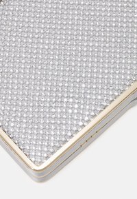 Hopea käärme, jossa on kultasävyinen kehys, peitetty riveillä pieniä, kiiltäviä, läpinäkyviä kivennäisiä valkoisella taustalla.