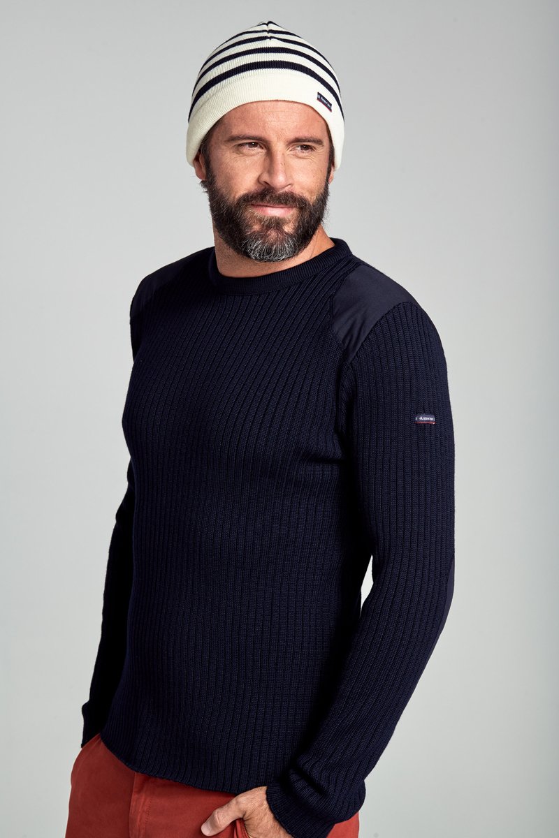 Pull en maille côtelée navy à manches longues, présentant un corps de couleur unie et des accents en tissu contrastant sur les épaules. Porté avec un bonnet rayé.