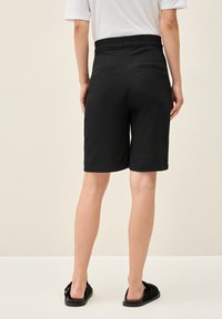 Svarta shorts med strukturerad yta, medellånga, med en bred midja och två bakfickor. Bärs med svarta sandaler.