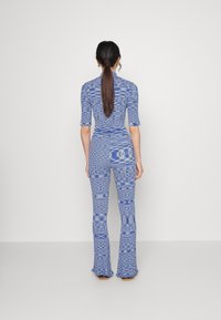 Combinaison à motifs bleus avec manches courtes, taille cintrée et pantalons évasés. Texture lisse avec un design multicolore sur l'ensemble.