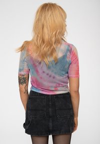 Sheer short-sleeve top with a tie-dye pattern in pink, purple, and blue, paired with a black denim mini skirt featuring back pockets.