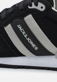 Juodas sportinis batelis su pilkais akcentais, tekstūruota zomša ir tinklelis, su „JACK & JONES“ logotipu šone ir raištelių užsegimu.
