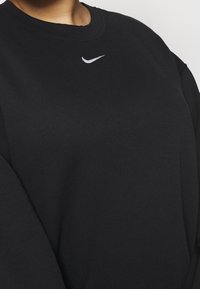 Černá mikina z texturované látky s kulatým výstřihem a dlouhými rukávy. Na hrudi je uprostřed malé bílé logo Nike.