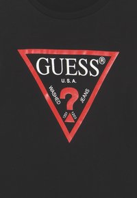Svart bomull T-skjorte med et stort rødt trekantlogo med "GUESS," "WASHED," "JEANS," og spørsmålstegn i hvitt.