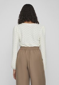 Haut à manches longues texturé blanc avec un motif en nid d'abeille, associé à un pantalon marron à taille élastique ; vu de dos.