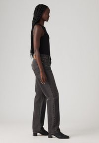 Zwarte tanktop gecombineerd met high-waisted, recht afgesneden donkergrijze jeans. Zwarte gewaagde enkellaarsjes zorgen voor extra lengte. Soepele textuur, minimalistisch ontwerp.