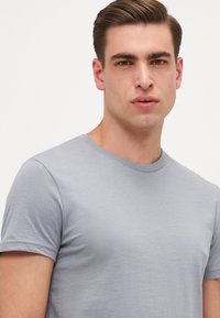 T-shirt en coton gris clair avec un col rond classique et des manches courtes, présentant une texture douce et un design simple.