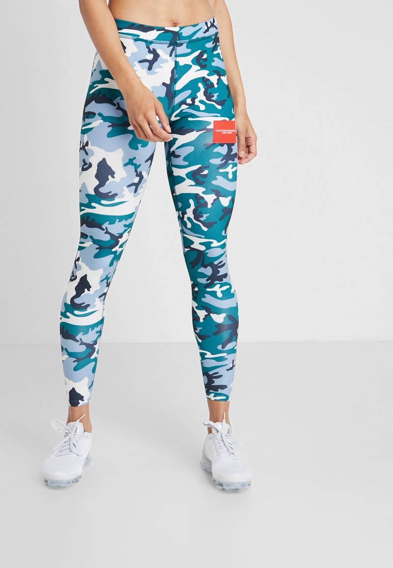 Leggings présentant un motif camouflage en teal, bleu et blanc. Fabriqués en tissu extensible avec une texture lisse et une taille légèrement haute.