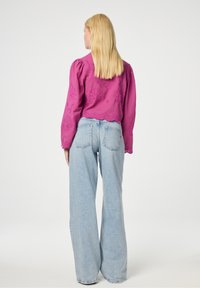 Fuchsia langemouwtop met bloemenborduursel en een geschulpte zoom, gecombineerd met lichtblauwe wijde jeans. Soepele textuur, ontspannen pasvorm.