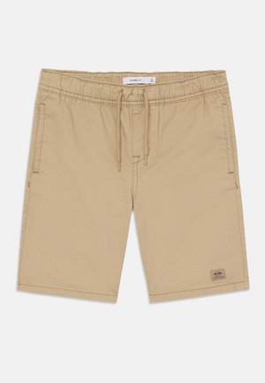 Bež kratke hlače s elastičnim pojasom, zatvorenjem na vezicu, bočnim džepovima i malom brendiranom oznakom blizu rubu. Glatka tekstura tkanine.