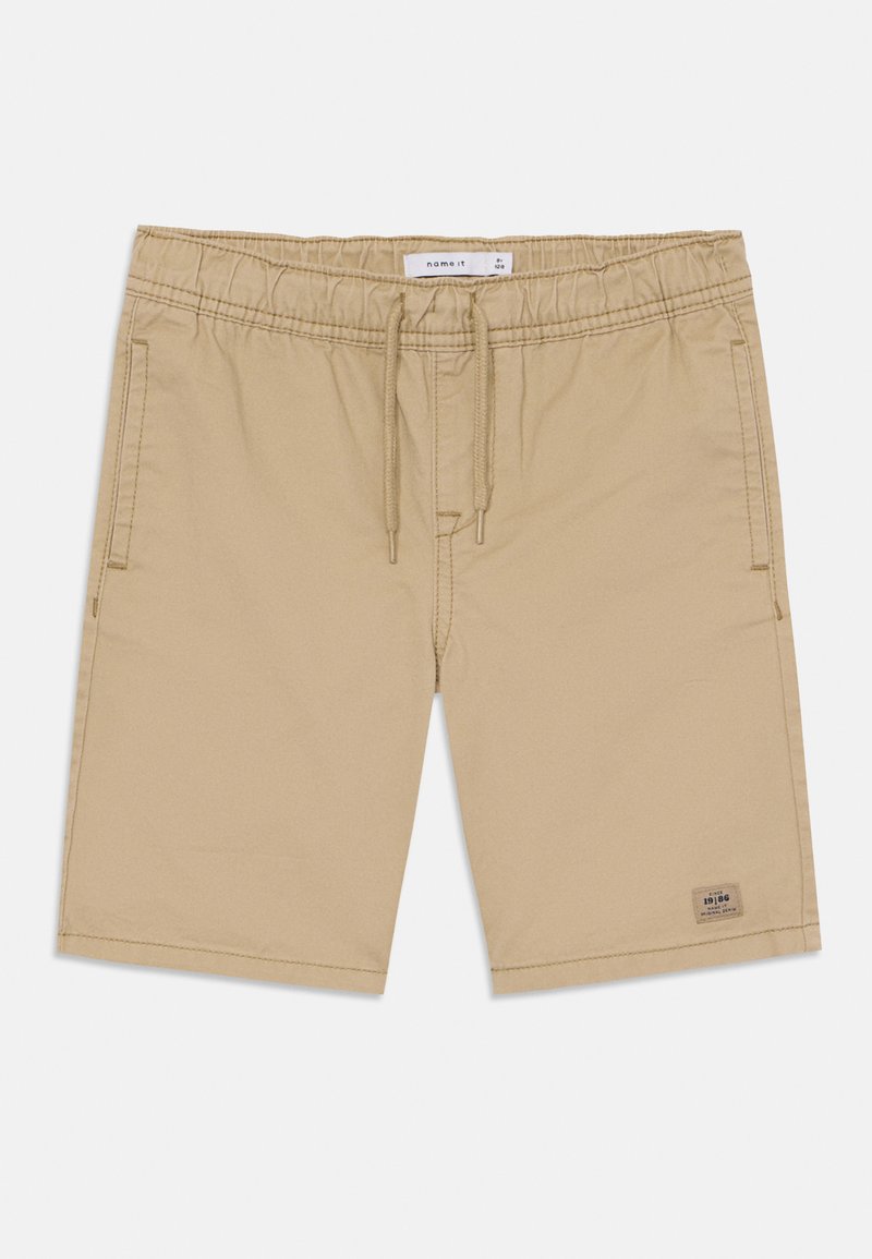 Shorts beiges avec une taille élastique, fermeture à cordon, poches latérales et une petite étiquette de marque près de l'ourlet. Texture de tissu lisse.