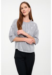 Top grigio con paillettes, scollatura rotonda e vestibilità morbida, con maniche corte e orlo leggermente accorciato. Indossato con pantaloni neri.