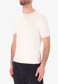 Maglione a maniche corte in crema con motivo testurizzato su un lato e finitura liscia dall'altro. Presenta un colletto rotondo e un'etichetta discreta.