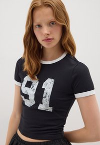 T-shirt nera a maniche corte con colletto bianco e stampa usurata bianca "91" sul davanti, stile aderente, tessuto dalla consistenza liscia.