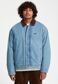 Lichtblauwe denimjas met een bruine corduroy kraag, drukknoopsluiting en zijzakken; voorzien van een klein logo op de borst.