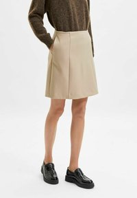 Beige knälång kjol med rak skärning, med sidfickor och subtila veck. Tillverkad i ett slätt tyg och kombinerad med svarta skor.