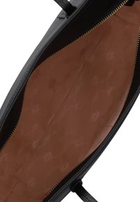 Zwarte handtas interieur met een gladde bruine voering, gouden ritsdetails en een subtiel gestikt patroon. Bevat een open, ruime indeling.