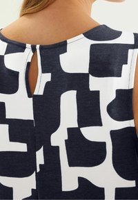 Tmavě modrý a bílý vzorovaný top s průstřihem v zadní části. Hladká látka s abstraktním vzorem a kulatým výstřihem.