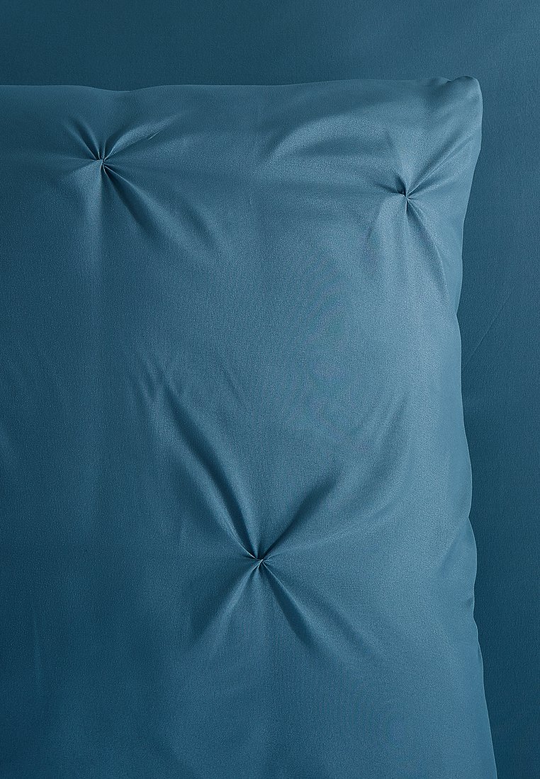 Dunkelblaues Kissen mit einer glatten Stoffoberfläche, das in der Mitte auffällige Absteppungen aufweist. Minimalistisches Design mit einer einheitlichen Farbe.