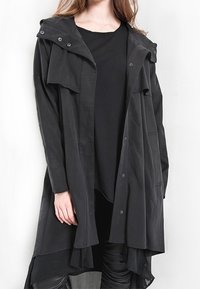 Langer schwarzer Mantel mit Kapuze, der über Knopfverschlüsse, ein drapiertes Design und einen strukturierten Stoff verfügt. Er hat einen lässigen Schnitt und seitliche Taschen.