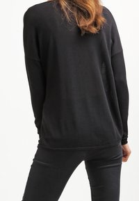 Czarny sweter dzianinowy o luźnym kroju, z długimi rękawami i zaokrąglonym dołem. Tył ma subtelną teksturę i swobodny design.