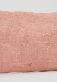 Prostokątny różowy poduszka z teksturowaną powierzchnią, z wytłoczonym logo "ESPRIT" w pobliżu dolnej krawędzi.