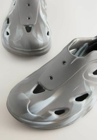 Grå slip-on sko med en glat, struktureret overflade, der har ventilationshuller og en afrundet form for komfort og åndbarhed.