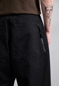 Pantalones cargo negros con un acabado texturizado, que cuentan con un bolsillo con cremallera lateral y un diseño de bolsillo trasero en forma de diamante.