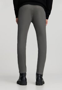 Pantaloni grigi a gamba stretta realizzati in tessuto testurizzato, dotati di due tasche posteriori con chiusura a bottone, indossati con stivali neri dalla suola spessa.