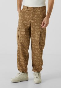 Pantaloni cargo maro cu un design repetitiv al logo-ului "KARL", cu mansete elastice și buzunare laterale. Asortați cu adidași albi.
