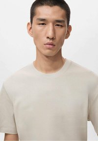 Beżowa koszulka z okrągłym dekoltem wykonana z miękkiego materiału. Posiada krótki rękaw i prosty, czysty krój bez widocznych logo czy wzorów.