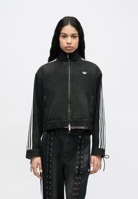 Μαύρο τζιν μπουφάν με ψηλό γιακά, εμπρός φερμουάρ και λευκές τρεις ρίγες στα μανίκια. Διαθέτει μικρό κεντημένο λογότυπο στο στήθος.