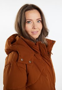 Barna, steppelt pufijacket kapucnival, ezüst patentos részletekkel és texturált szövet részletekkel. Cipzáros elülső záródás.