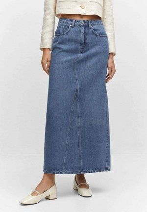 Kvinde iført et højtaljet, ankel-lang blå denimnederdel med syninger foran, kombineret med cremefarvede lavhælede sko og cropped beige jakke.