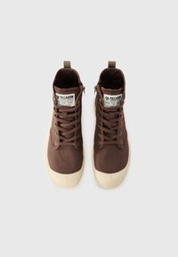 Zapatillas altas de tela marrón con una puntera de goma crema, cordones en la parte delantera y cremallera lateral. Presentan etiquetas de la marca en la lengüeta.