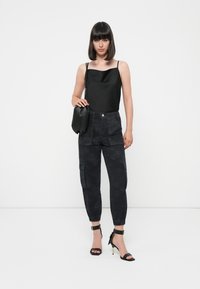 Zwarte satijnen cami-top, hooglopende cargo-broek met een donker camouflagepatroon en zwarte strapschoenen. Accessoires: kleine zwarte tas.