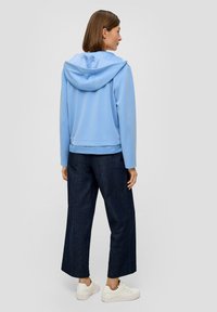  Lichtblauwe hoodie met lange mouwen, een ontspannen pasvorm en een geribde onderrand, gecombineerd met donkere wijde jeans en witte sneakers.