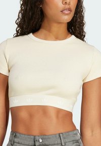 Heled kreemjas ribaga lühikesed varrukad ja sobiv disain. Omab bränditud elastset vanti lillemustritega ääres.