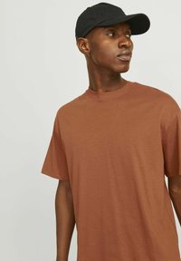 Brun bomulds T-shirt med rund hals og korte ærmer, parret med en sort kasket. Glat tekstur og afslappet pasform.