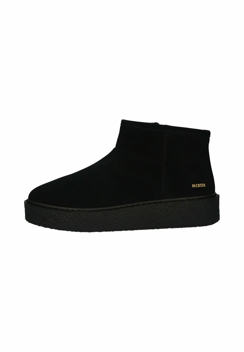 Botas de tobillo de ante negro con un diseño alto, suela de plataforma negra texturizada y sutil branding dorado en el lateral. Acabado suave, diseño sencillo.