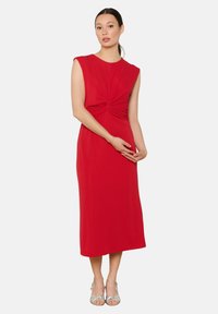 Vestido rojo sin mangas con un corpiño ajustado y detalles fruncidos en la cintura, que fluye hacia una falda midi de tela suave.
