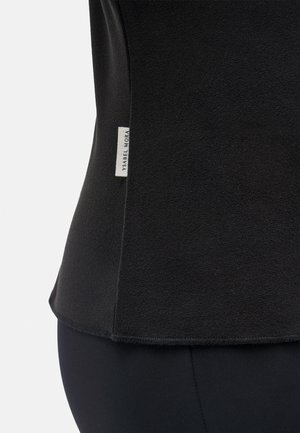 Top negro de tela suave con textura lisa, que cuenta con una etiqueta en la costura lateral con "Ysabel Mora". Dobladillo curvado en la parte inferior.