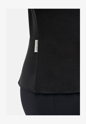 Top negro de tela suave con textura lisa, que cuenta con una etiqueta en la costura lateral con "Ysabel Mora". Dobladillo curvado en la parte inferior.