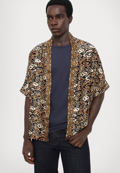 Krátký rukáv, černá a zlatá vzorovaná košile s vířivými designy, zdobená kontrastním límcem a lehkým materiálem. Nasazená přes námořnickou košili.