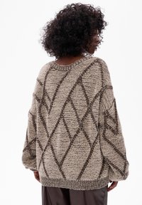 Przytulny, większy sweter z dzianiny w kolorze beżowym, ozdobiony wzorem w diamenty, z teksturowanym wykończeniem i ściagaczem u dołu. Długie rękawy i luźny krój.
