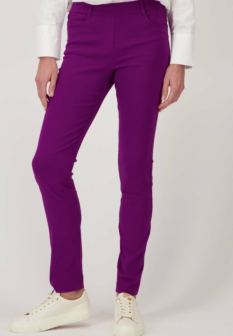 Paasvormige paarse stretchbroek met zakken, gecombineerd met witte sneakers. Gladde textuur en een op maat gemaakt ontwerp voor een gestroomlijnde uitstraling.