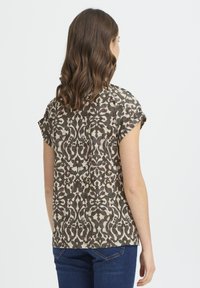 Hátsó nézet egy barna és krémszínű virágmintás rövid ujjú blúzról, laza szabással és puha, texturált anyagból.