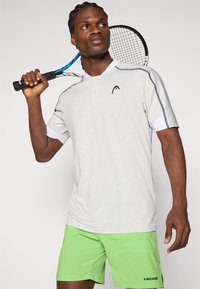 Camisa polo gris con cuello blanco, mangas cortas, logo negro y acentos azules contrastantes; combinada con pantalones cortos verdes que presentan un logo de la marca.