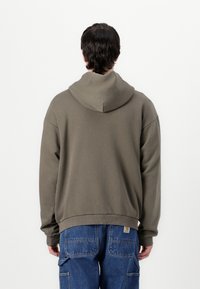 Olive green hoodie, cotton blend, relaxed fit, kangaroo pocket, drop shoulders, ribbed cuffs and hem, back view. Paired with blue cargo pants.